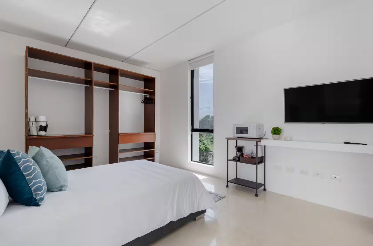 A modern bedroom with a bed, a TV, a desk, and a window.
