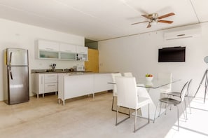A modern kitchen with a refrigerator, microwave, and white cabinets. There is a dining table with chairs and a ceiling fan. - Residencial Palmaris by Homirent (Cancún)