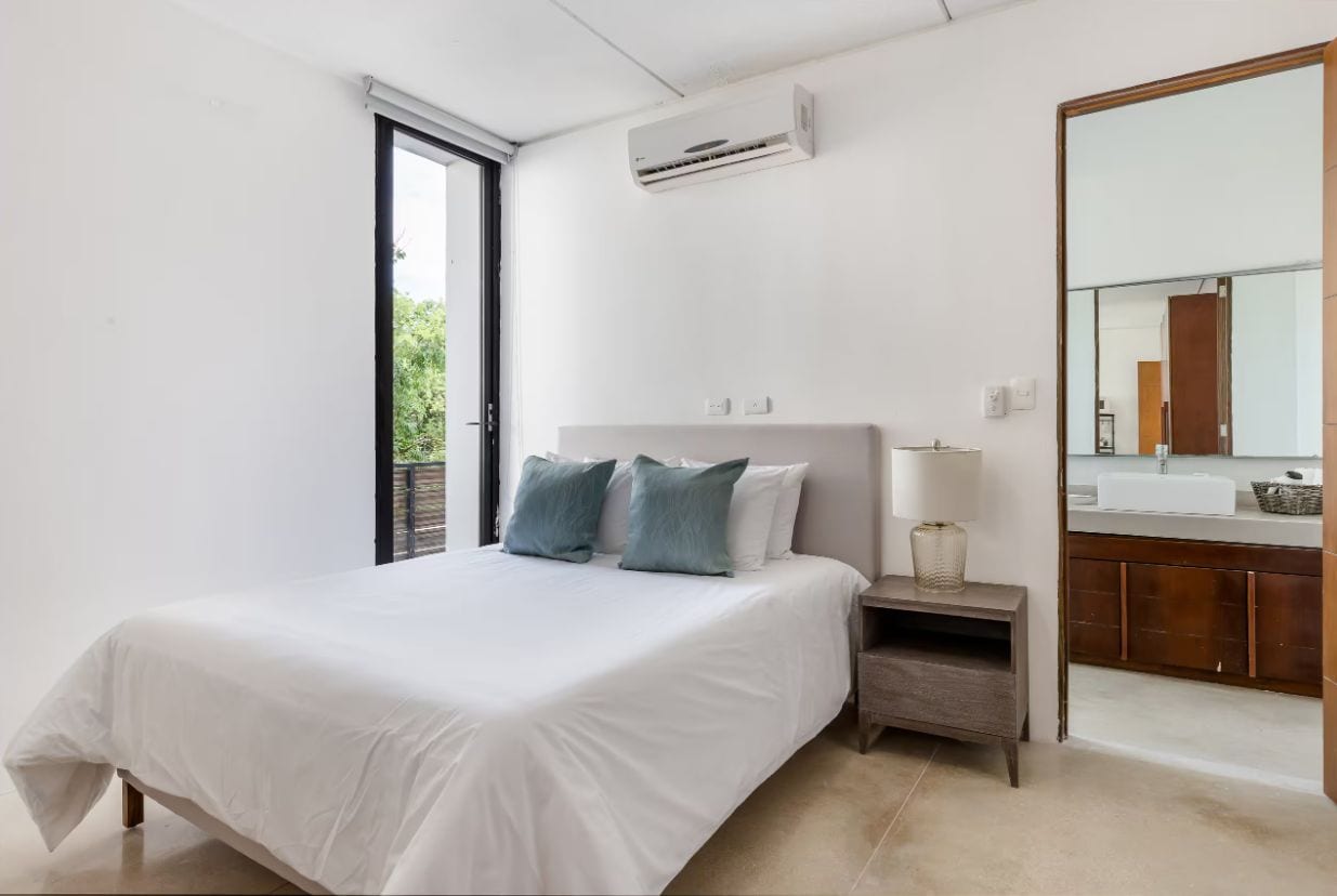 A bedroom with a bed, bedside table, lamp, and a large mirror.