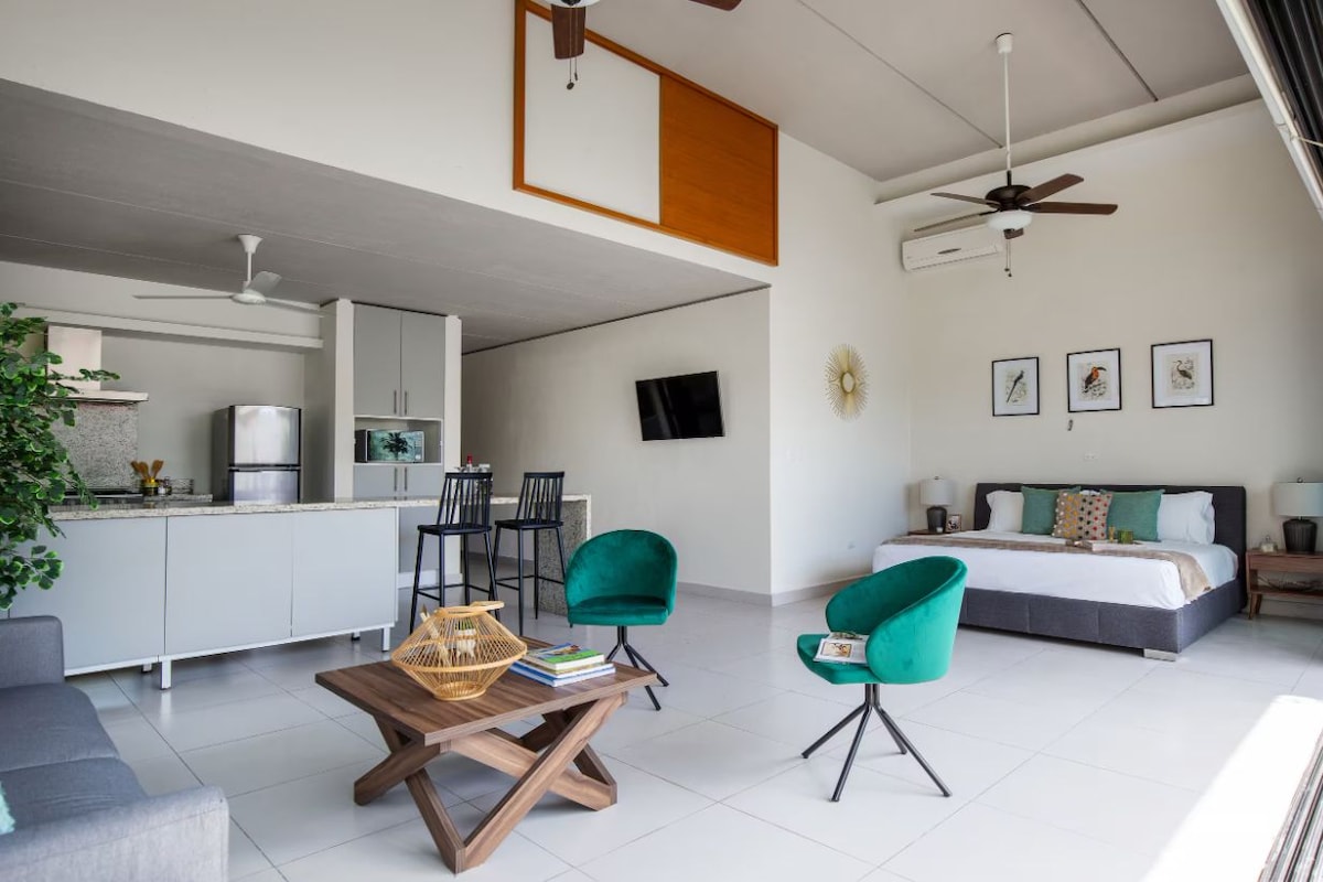 A modern hotel room with a bed, a desk, and a seating area with chairs.