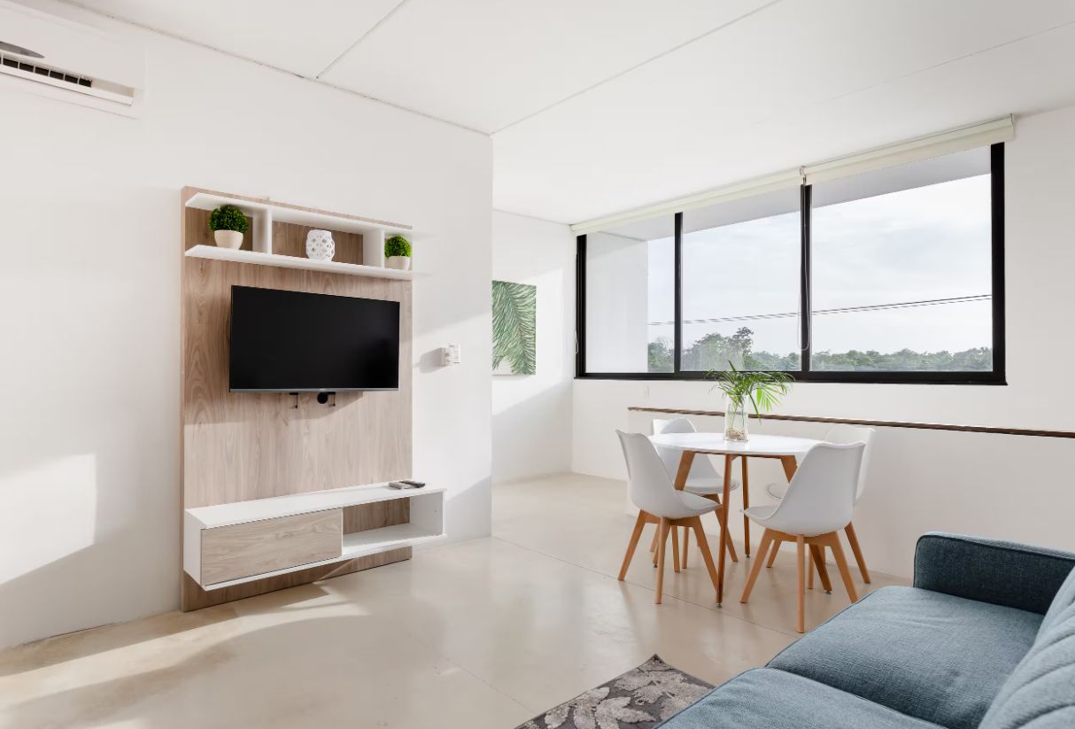 Un soggiorno moderno con TV a schermo piatto, un'area pranzo con tavolo e sedie bianche e un'ampia finestra vista.