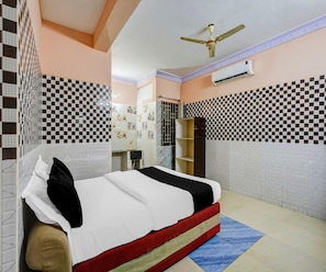 A hotel room with a bed, a ceiling fan, an air conditioning unit, and patterned walls.