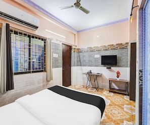 Una habitación de hotel con cama, televisión, una mesita y ventilador de techo.