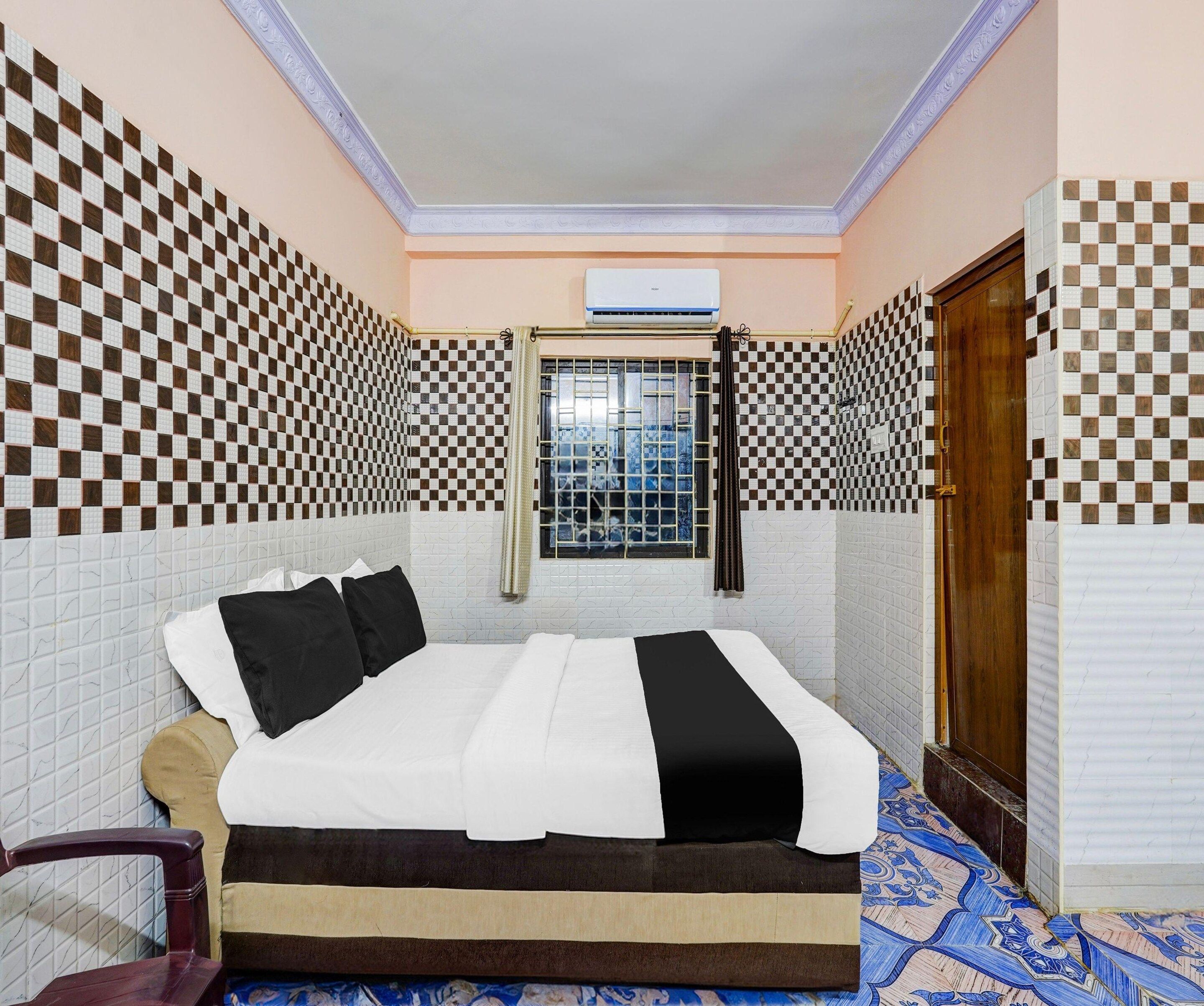 A bedroom with a checkered wall pattern, a bed with white and black bedding, a window with a view, and a wooden door.