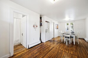 A room with a wooden floor, white walls, a dining table with chairs, and a door leading to another room. - Perfect Family Beach Getaway (Old Orchard Beach)