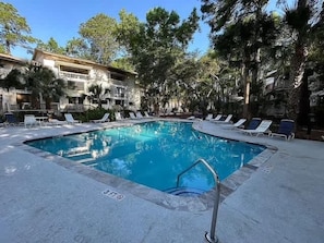 A rectangular swimming pool with a metal ladder, surrounded by lounge chairs and trees. - Seascape Hideaway - Steps to Beach - Suite (Hilton Head Island)