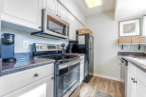 A modern kitchen with stainless steel appliances, white cabinetry, and a granite countertop. - Seascape Hideaway - Steps to Beach - Suite (Hilton Head Island)
