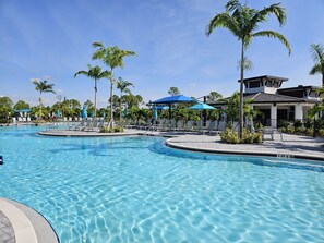 A swimming pool with lounge chairs and umbrellas, surrounded by palm trees and a building with a white facade. - Luxury Vacation Townhome in Wellen Park Golf & Country Club (Venice)