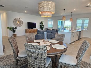 A modern kitchen with a central island, a dining area with wicker chairs, and a living room with a gray sofa. - Luxury Vacation Townhome in Wellen Park Golf & Country Club (Venice)