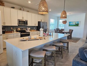 Una cucina moderna con mobili bianchi, elettrodomestici in acciaio inossidabile e una grande isola con sgabelli da bar.