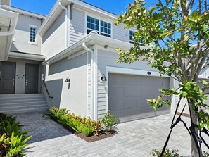A residential building with a garage, a front door, and a small garden area with plants. - Luxury Vacation Townhome in Wellen Park Golf & Country Club (Venice)