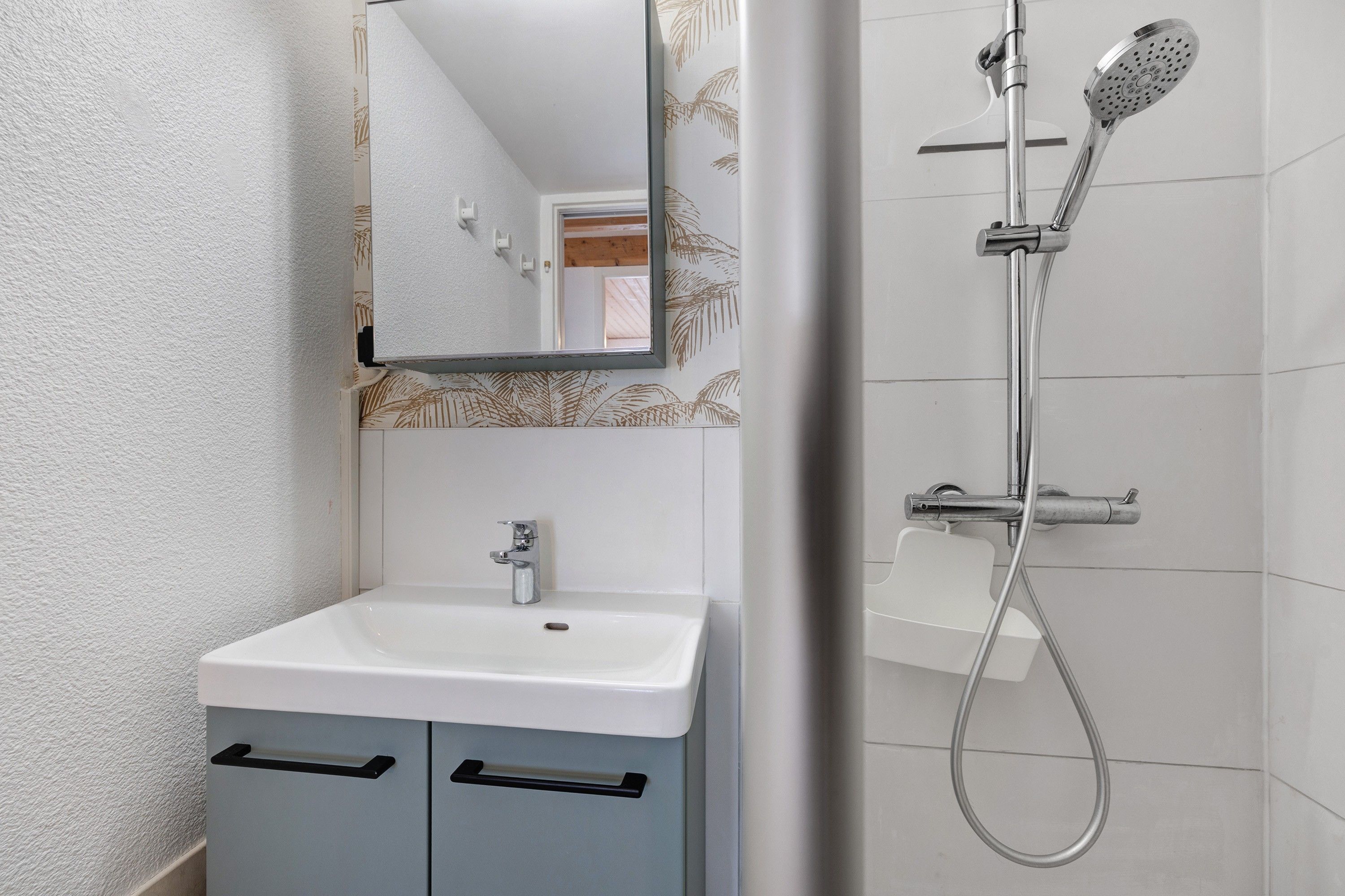 Ein Badezimmer mit einem weißen Waschbecken, einem Spiegel und einer Dusche mit Duschbrause.
