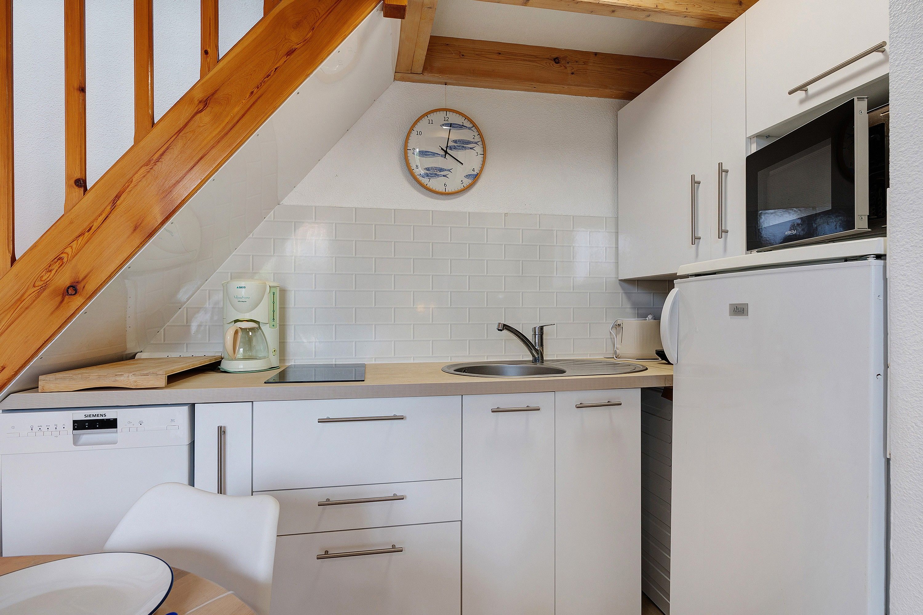 Een kleine keuken met witte kasten, een ingebouwde magnetron, een koffiezetapparaat en een houten plafond.