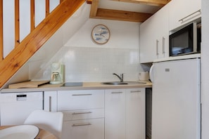 A compact kitchen with white cabinets, a built-in microwave, a coffee maker, and a wooden ceiling.