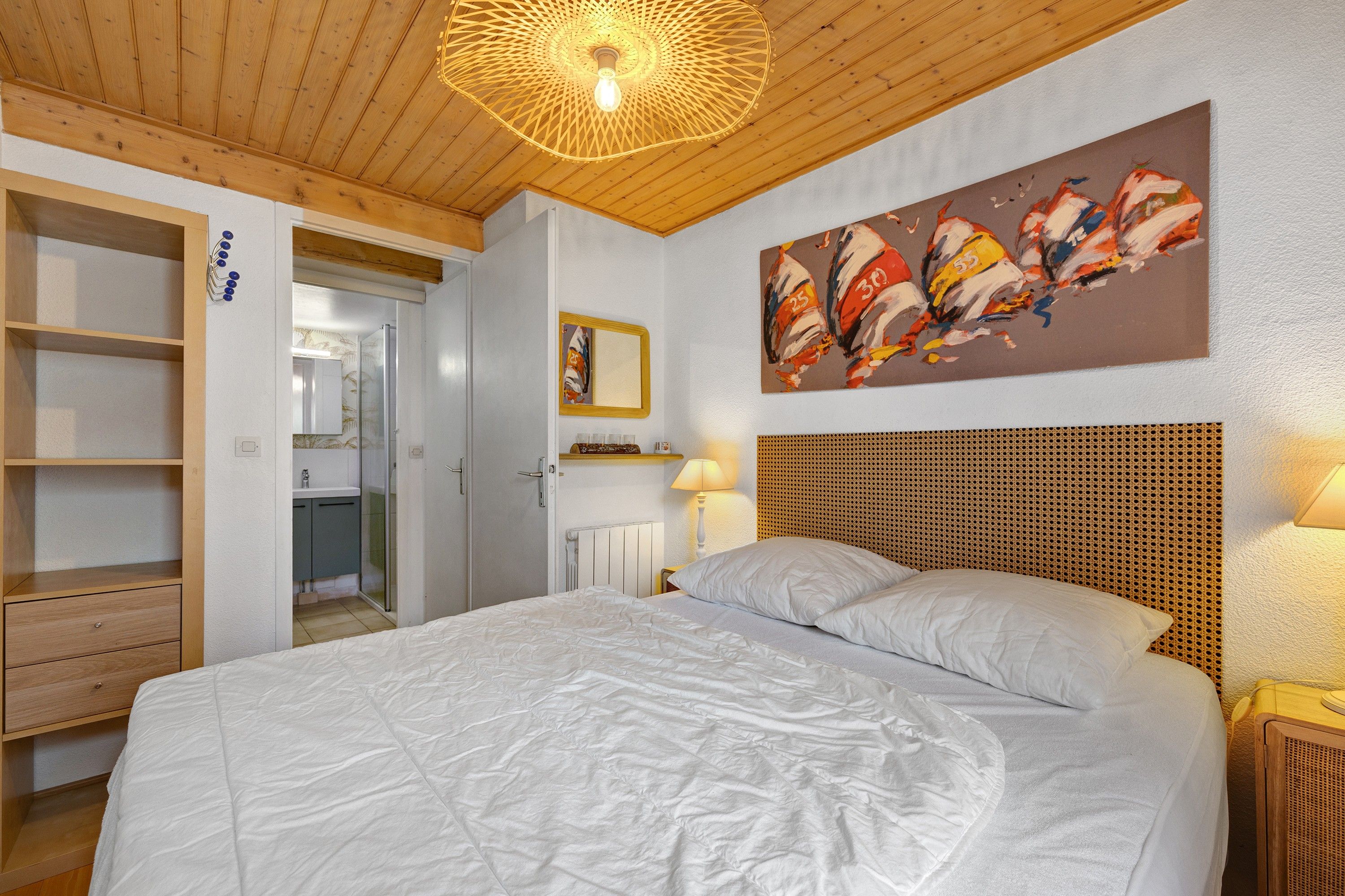 Een slaapkamer met een bed, een houten hoofdbord, een schilderij en een plafondlamp.