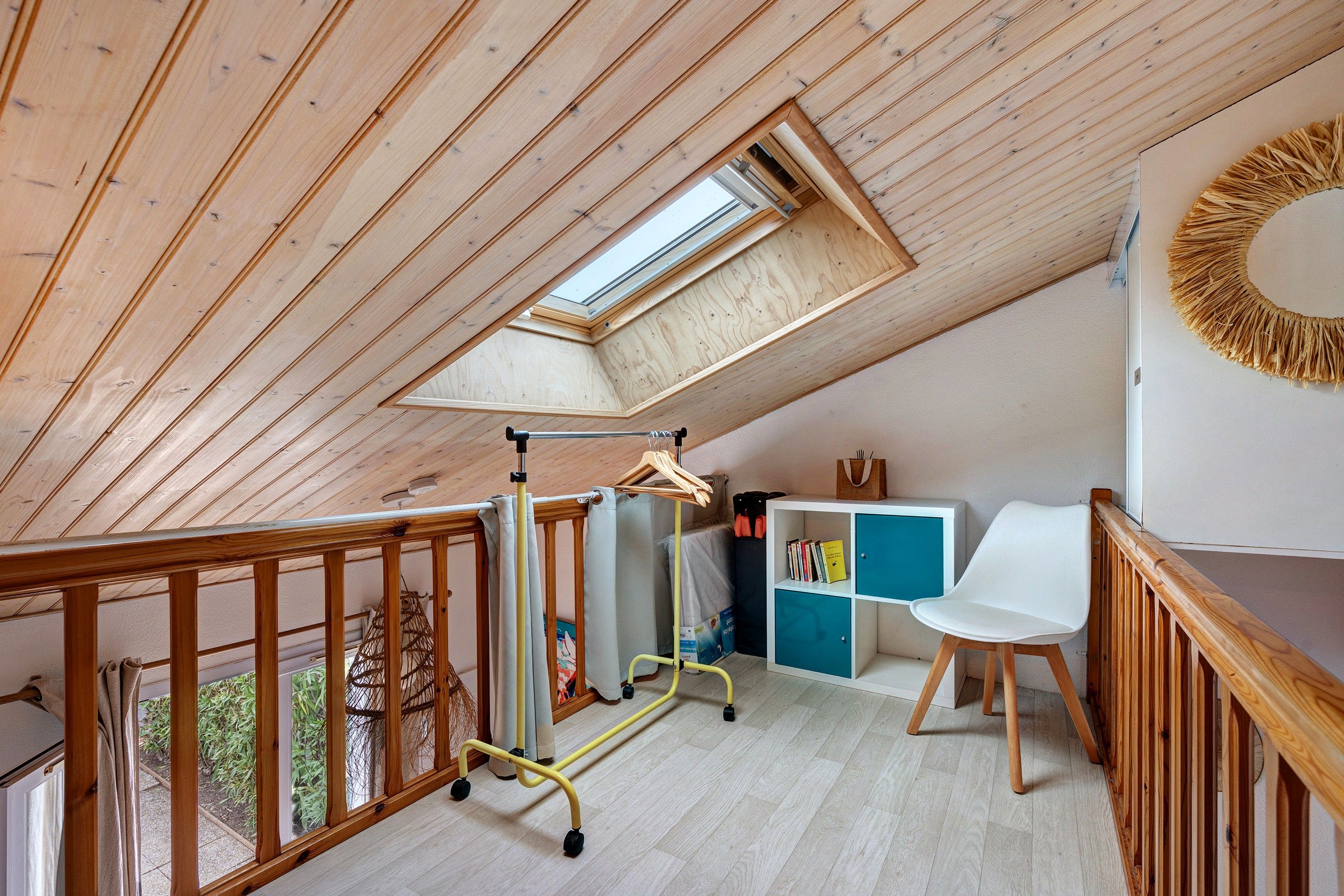Een kamer met een schuine plafond, een houten wieg, een witte stoel en een klein bureau met een blauwe kast.