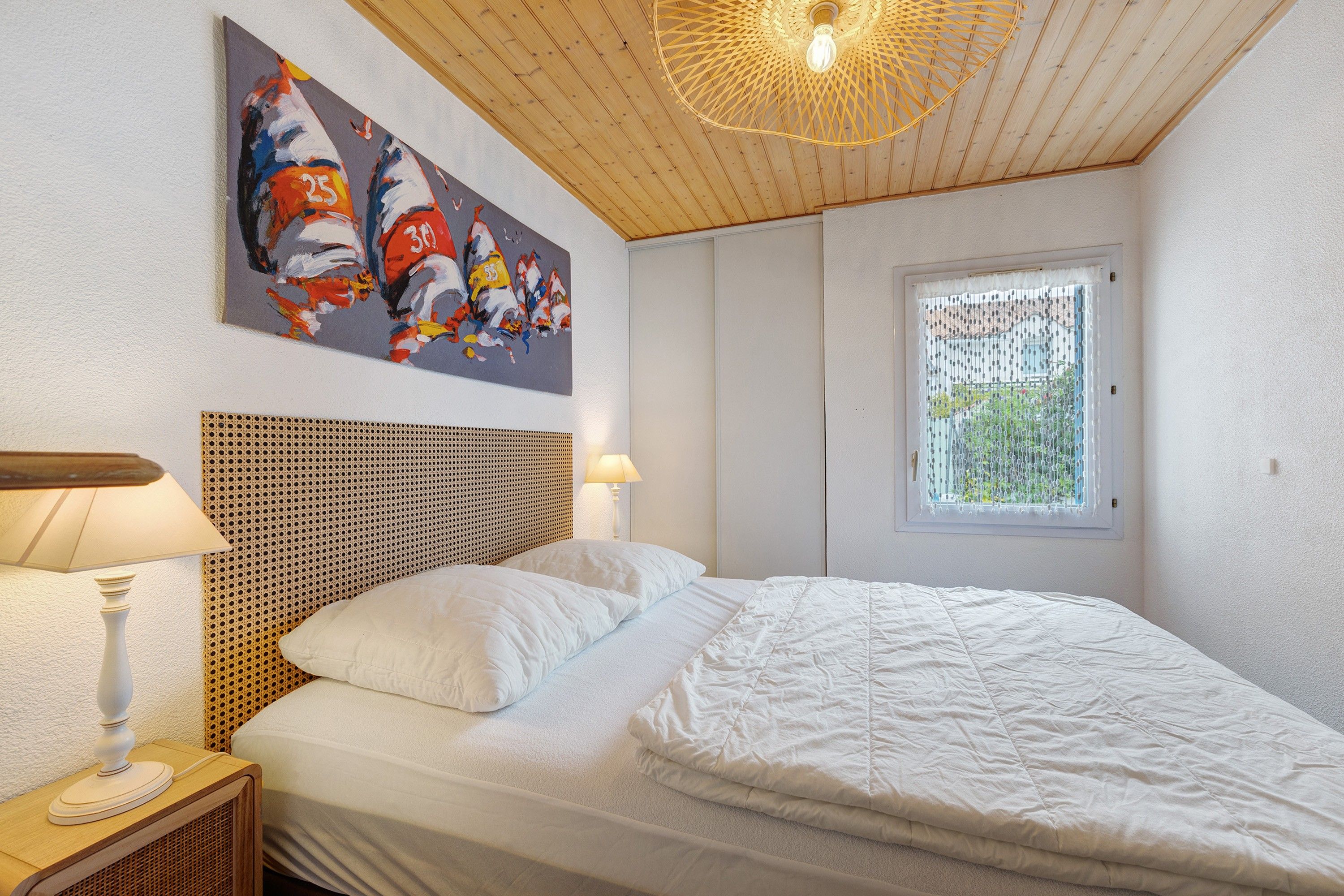 Ein Schlafzimmer mit einem Bett, einem Nachttisch, einer Lampe, einem Wandbild, einem Fenster mit Blick und einer Holzboden.