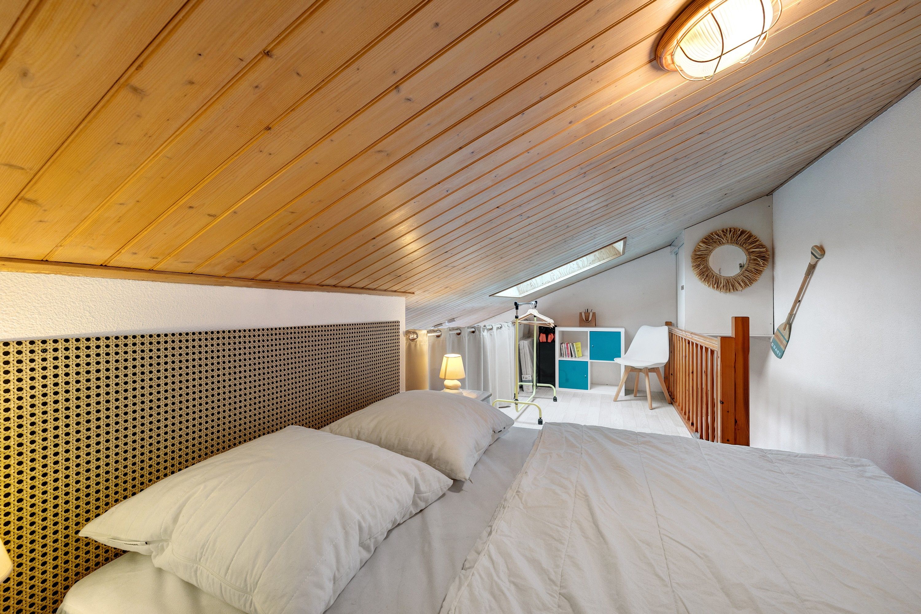 Een slaapkamer met een schuine kap, een bed met witte beddengoed, een houten hoofdbord en een spiegel aan de muur.