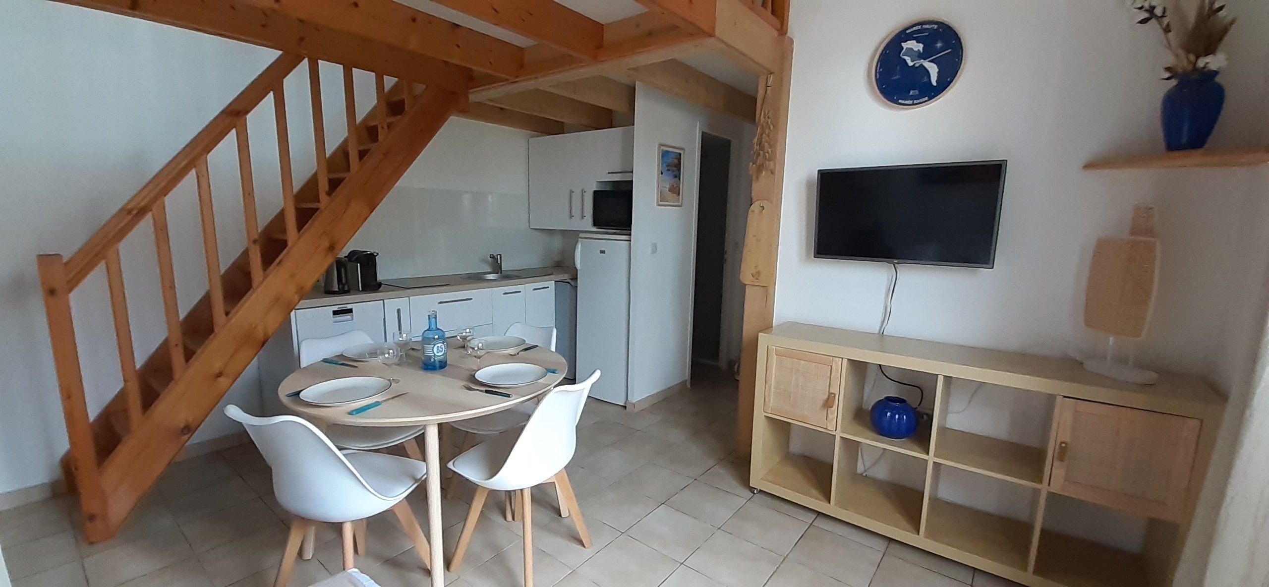 Cocina compacta con comedor, escalera de madera y un televisor de pantalla plana en un estante.