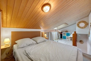 A bedroom with a wooden ceiling, a bed with white bedding, a bedside lamp, and a small window.