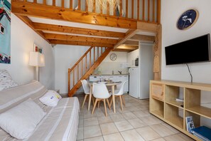 A cozy room with a bed, a dining table with chairs, a kitchen area, and a TV mounted on the wall.