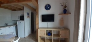 Ett kök med vita skåp, en mikrovågsugn och ett kylskåp. Det finns en hylla i trä med en klocka och en vas med torkade växter.