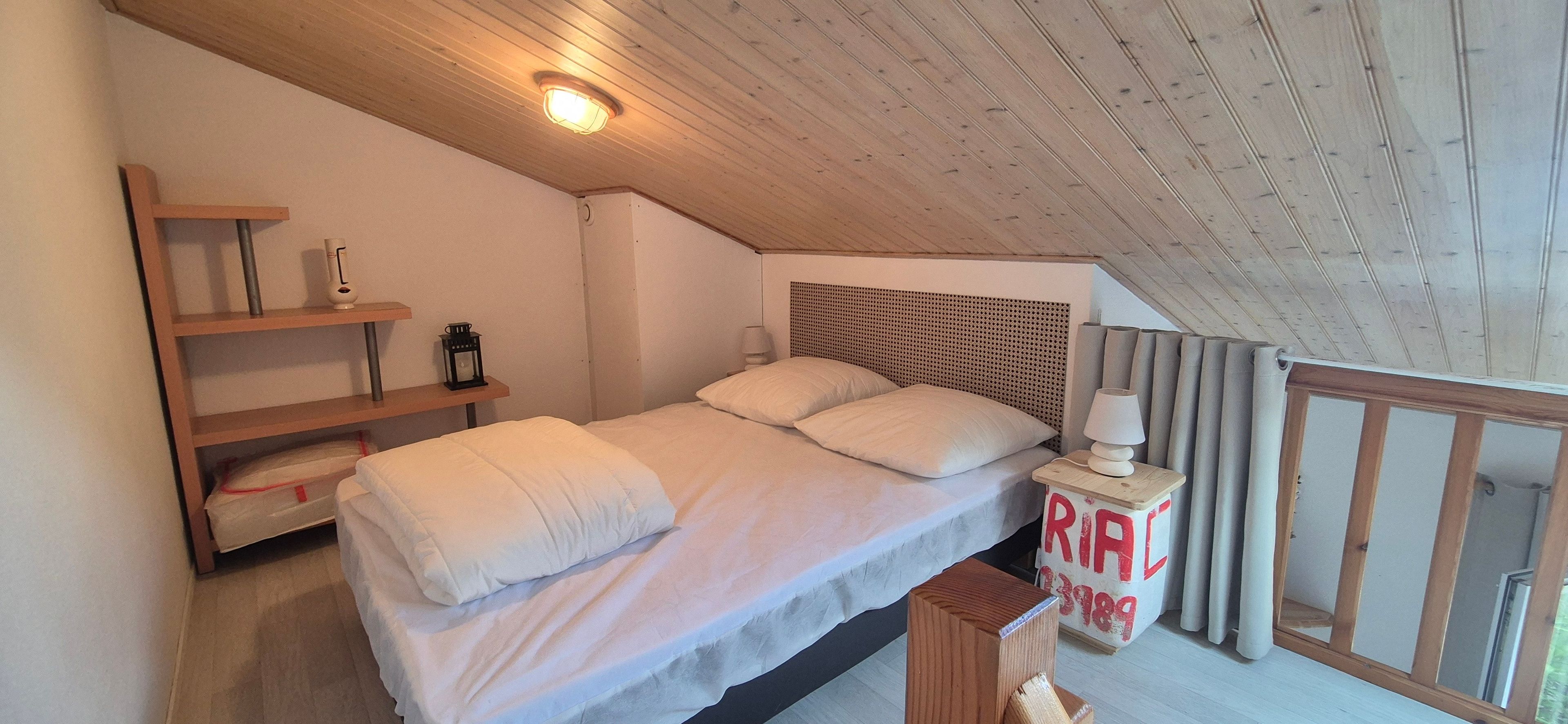Ett sovrum med en säng, en sänggavel i trä, sänglampor och en hylla med diverse föremål.