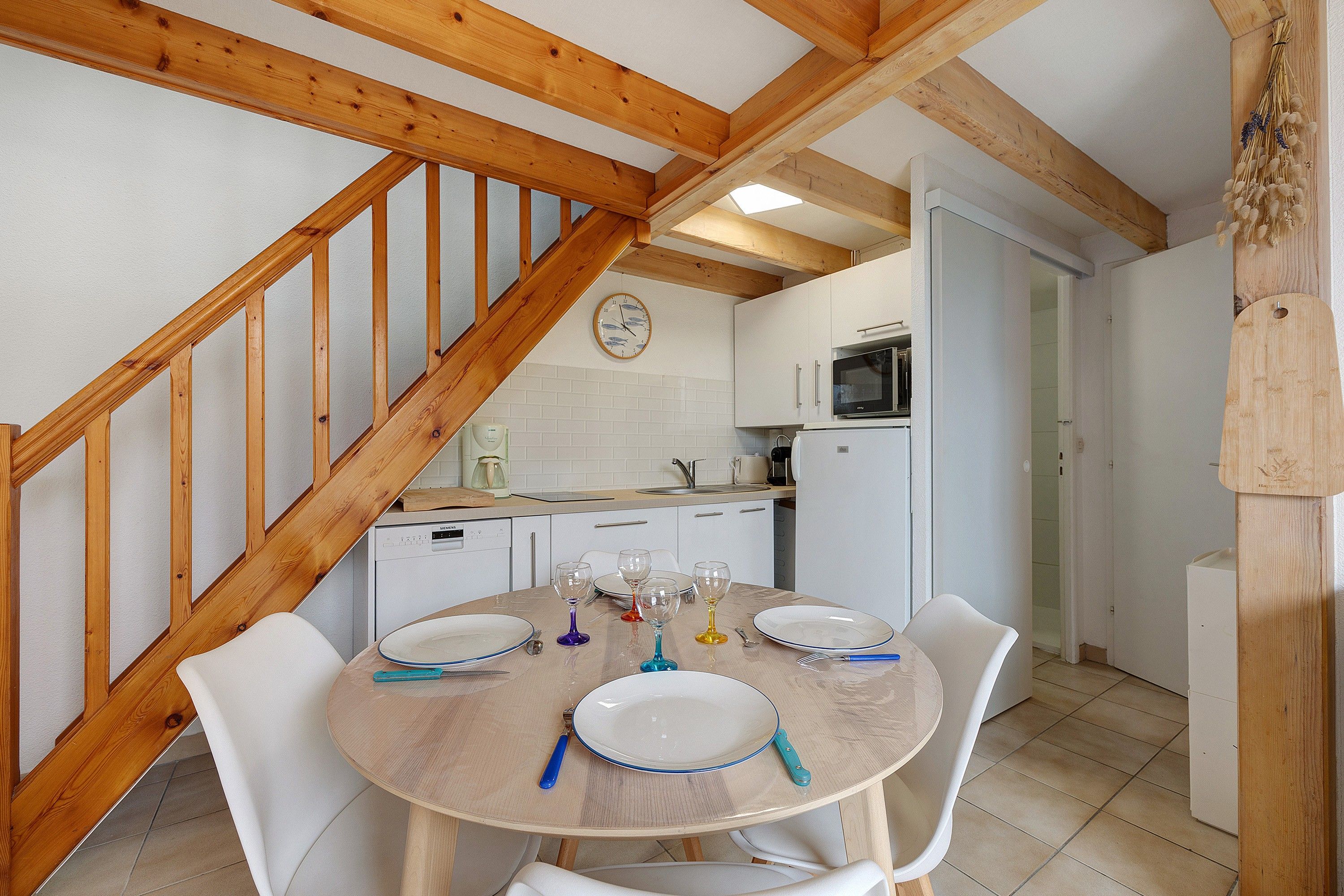 A dining area with a wooden table, white chairs, and a kitchen in the background.
