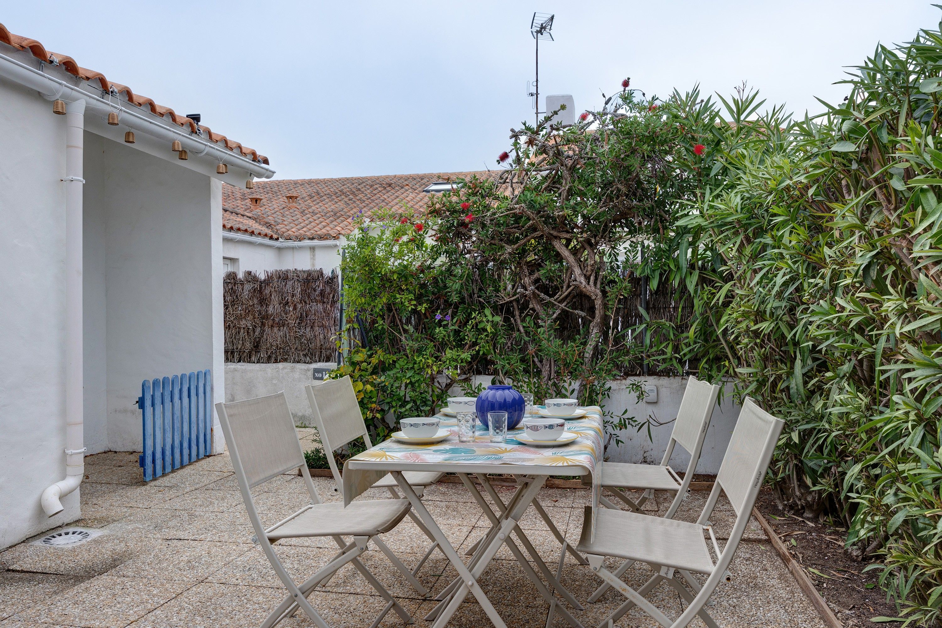 An outdoor patio with a table set for dining, surrounded by chairs, and a blue vase on the table.