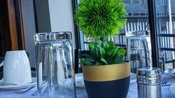 Una mesa con una planta en maceta, un jarro de vidrio y un recipiente metálico.