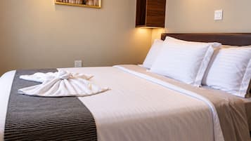 A hotel room with a neatly made bed, a towel on the bed, and a wall-mounted light.