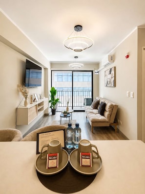 A modern living room with a sofa, a coffee table, a TV, and a dining area with two plates of McColin's tea and water bottles. - 2 dormitorios San Isidro AC y coworking (Lima)