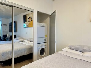 A hotel room with a bed, a washing machine, a desk, and a television. - Cozy 3 Beds Suite (Toronto)