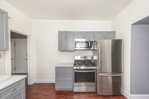 A compact kitchen with grey cabinets, a stainless steel refrigerator, a microwave, and a stove. - Spacious 4BR Newark Stay,EWR, Seton Hall + NYC (Newark)