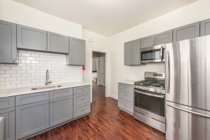 A modern kitchen with grey cabinets, a stainless steel refrigerator, a built-in oven, and a microwave. - Spacious 4BR Newark Stay,EWR, Seton Hall + NYC (Newark)