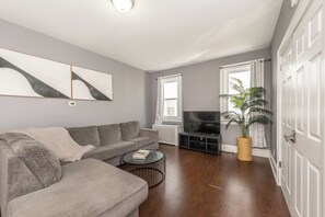 A living room with a grey sofa, a coffee table, a flat-screen TV, and a potted plant. - Spacious 4BR Newark Stay,EWR, Seton Hall + NYC (Newark)