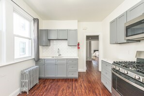 A modern kitchen with grey cabinets, a white tiled backsplash, a stainless steel range hood, and a wood floor. - Spacious 4BR Newark Stay,EWR, Seton Hall + NYC (Newark)