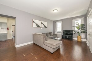 A living room with a grey sofa, a coffee table, a flat-screen TV, and a potted plant. - Spacious 4BR Newark Stay,EWR, Seton Hall + NYC (Newark)