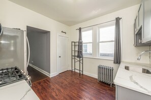A kitchen with a gas stove, a built-in oven, a white countertop, a sink, and a window with blinds. - Spacious 4BR Newark Stay,EWR, Seton Hall + NYC (Newark)