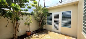 A narrow outdoor corridor with a potted plant, a door with horizontal slats, and a wall with climbing plants. - Private 2BD/2BA Rear Casita in Guaynabo (Guaynabo)