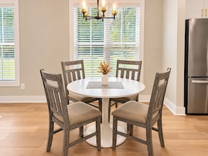 A dining area with a round table, four wooden chairs, a chandelier, and a refrigerator. - The Haven at Holly Springs (Holly Springs)