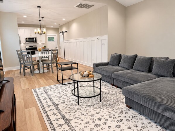 A modern living room with a grey sofa, a round coffee table, and a dining area with a white table and chairs.
