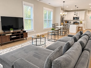 A modern living room with a large grey sofa, a flat-screen TV, and a wooden entertainment unit. - The Haven at Holly Springs (Holly Springs)