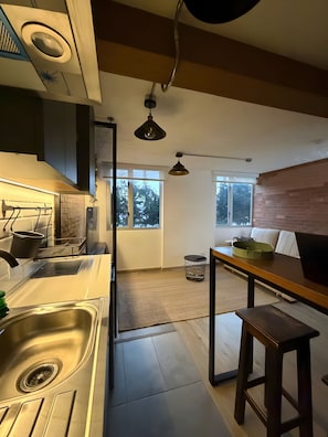 A modern kitchen with a stainless steel sink, a wooden dining table, and a black pendant light. - Vrbo Property (Bogotá)