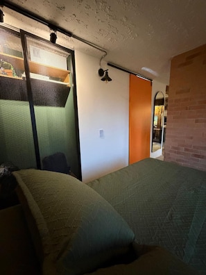 A bedroom with a bed, a sliding door, a small table, and a wall-mounted light fixture. - Vrbo Property (Bogotá)