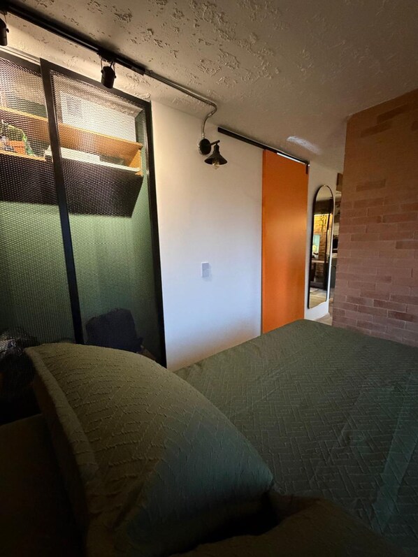 A bedroom with a bed, a sliding door, a small table, and a wall-mounted light fixture. - Vrbo Property (Bogotá)