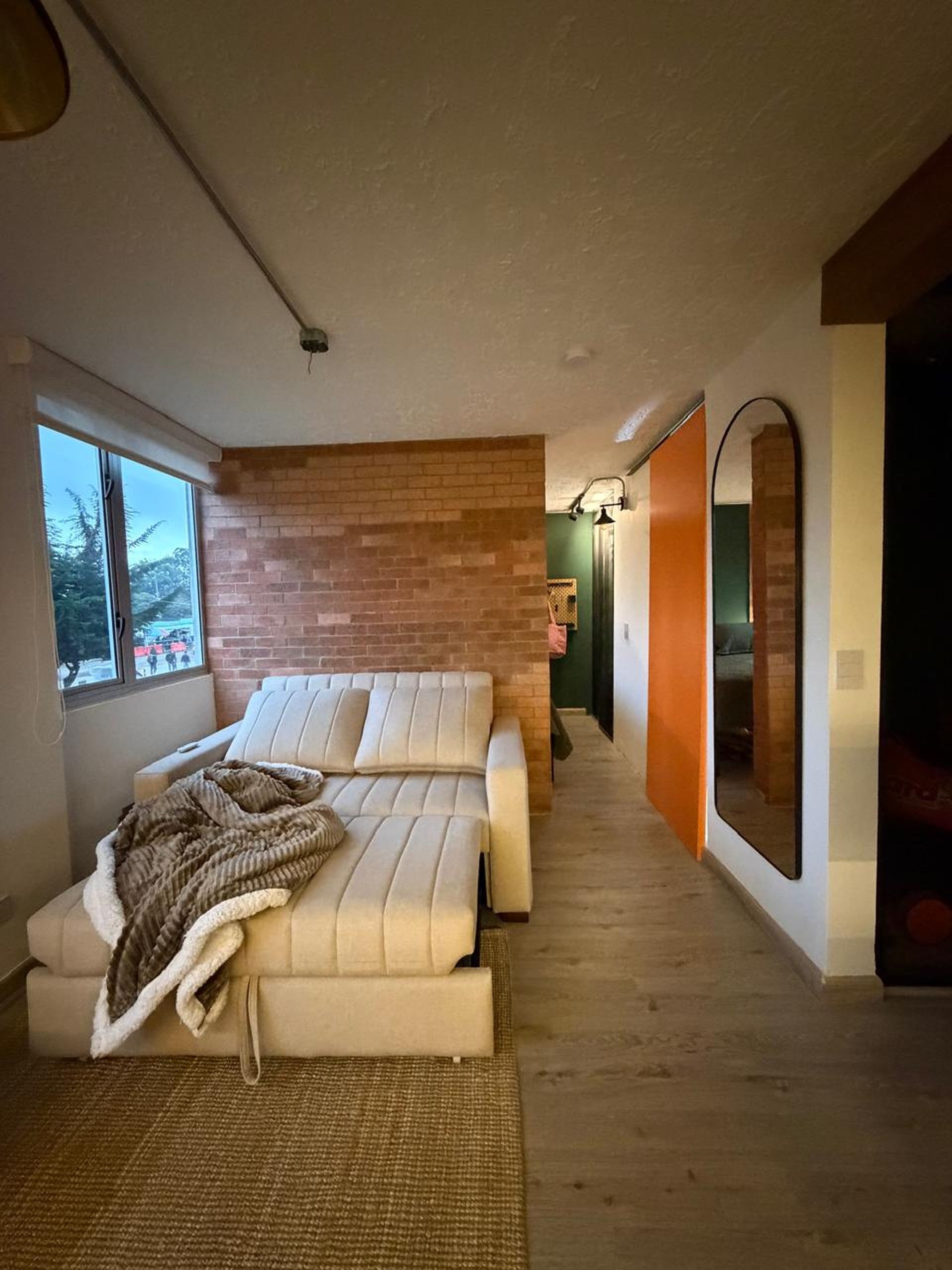 A modern bedroom with a brick accent wall, a large window, and a view of the outside.