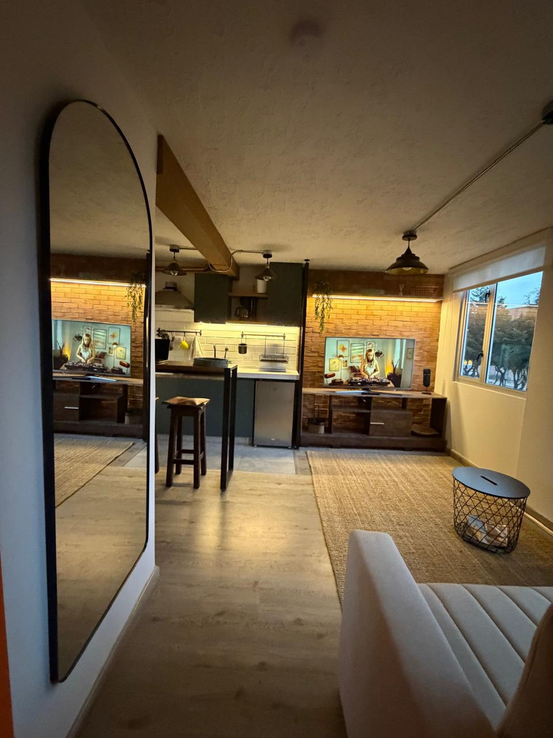 Una cocina moderna con una isla central, una zona de comedor con sofá y un espejo grande que refleja el ambiente.