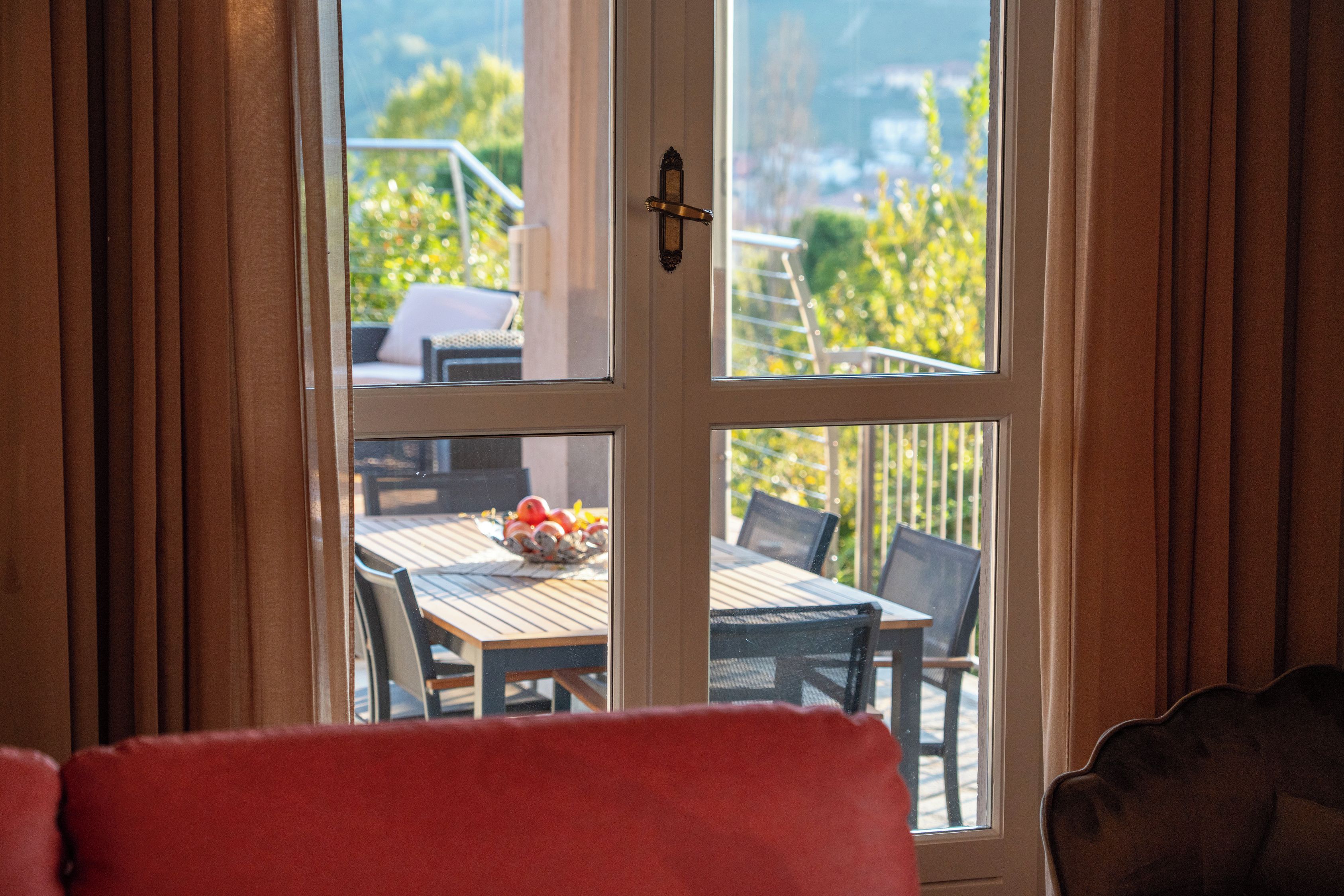 Una stanza con vista tramite una porta vetrata, un tavolo da pranzo con sedie e una poltrona rossa in primo piano.