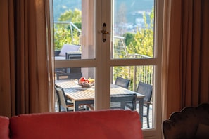 A room with a view through a glass door, a dining table with chairs, and a red chair in the foreground. - Sinfonia di Langa - Three Bedroom Villa, Sleeps 6 (Alba)